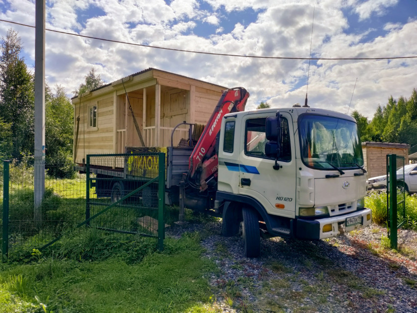 Грузовик с краном-манипулятором привёз деревянный домик на ограждённый дачный участок