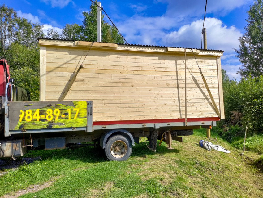 Деревянный модульный домик на платформе грузовика, закреплённый ремнями в сельской местности