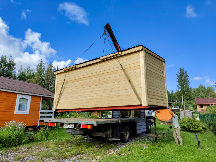 Рабочий удерживает деревянный модульный дом при подаче краном-манипулятором на место установки