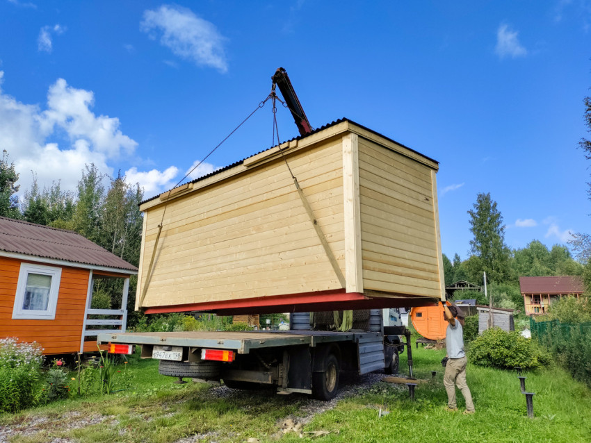 Рабочие направляют подвешенный деревянный модуль при разгрузке краном-манипулятором