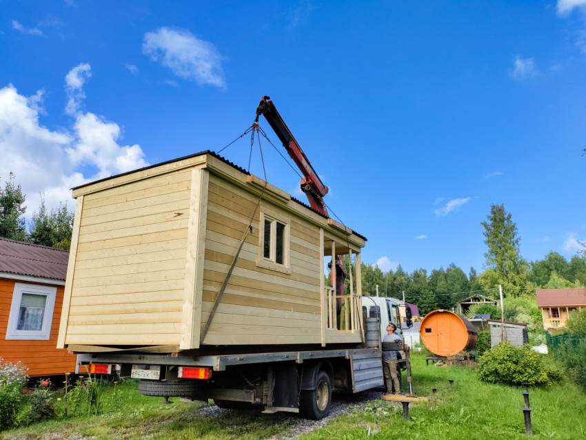 Рабочий контролирует разгрузку деревянного модуля на платформе грузовика с краном-манипулятором