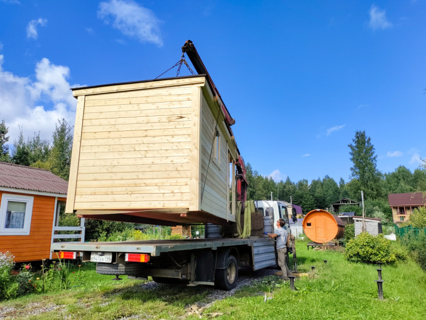 Деревянный модульный дом поднят краном-манипулятором над дачным участком во время монтажа