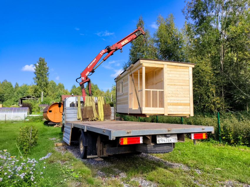 Кран-манипулятор поднимает модульный домик над грузовой платформой