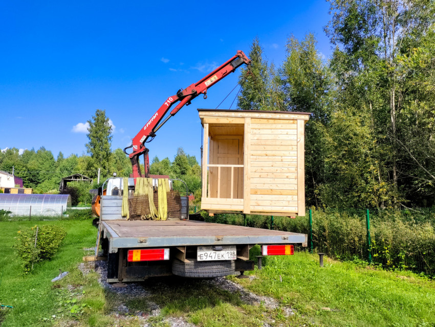 Грузовик с краном-манипулятором поднимает деревянный модуль на дачном участке