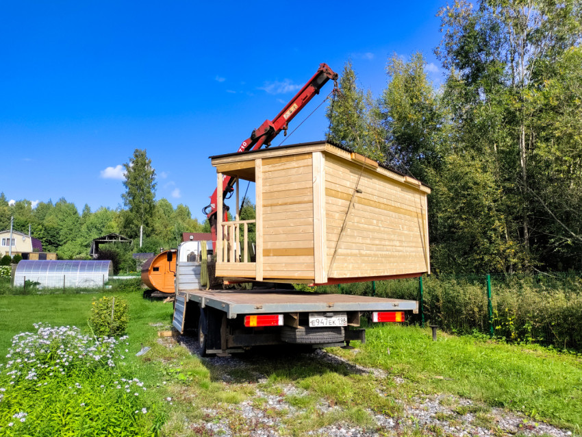 Подвешенный деревянный модульный дом перемещают краном-манипулятором над зелёным участком