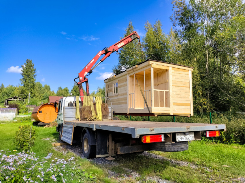 Подъём деревянного домика краном-манипулятором на фоне деревьев