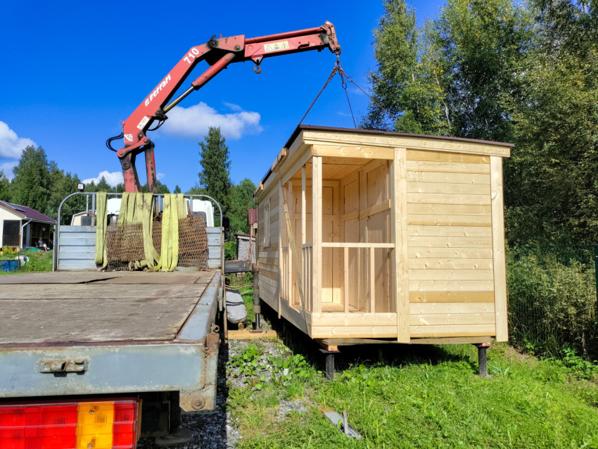Манипулятор опускает деревянный модуль на площадку среди деревьев и травы