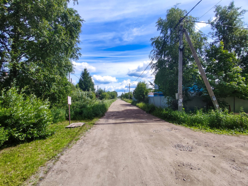 Прямая грунтовая дорога с опорами связи и воздушными проводами в частном секторе