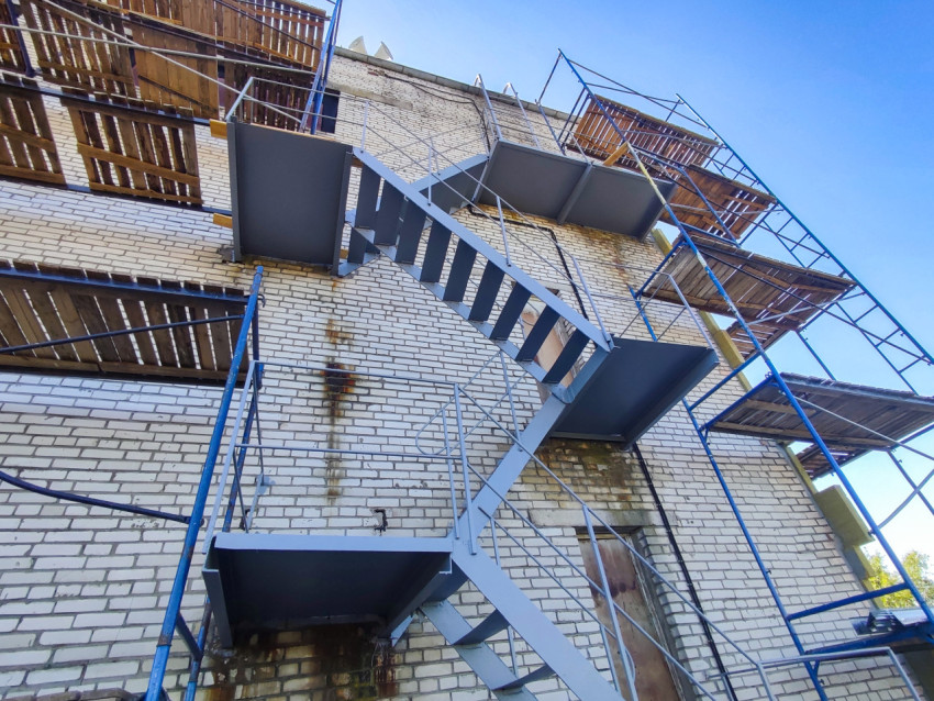 Наружная металлическая лестница на кирпичном здании в процессе фасадных работ