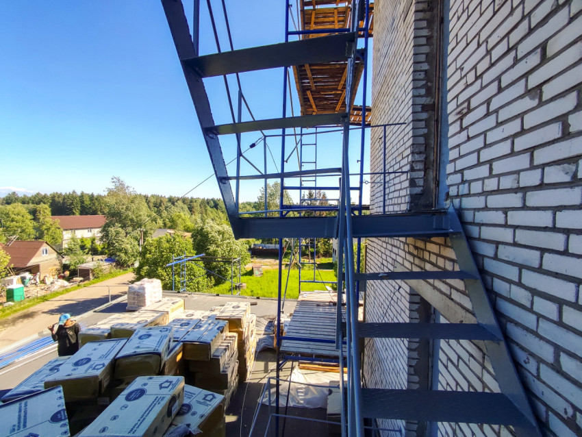 Строительные леса у белой кирпичной стены и штабель упакованного утеплителя на кровле