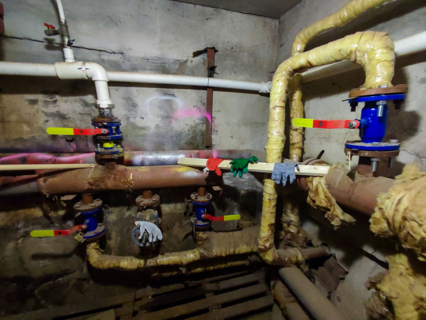 Ряд шаровых кранов на трубах в подвале, рабочие перчатки на деревянной рейке