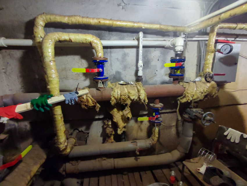 Инженерный узел с кранами, манометром и повреждённой теплоизоляцией в подвале