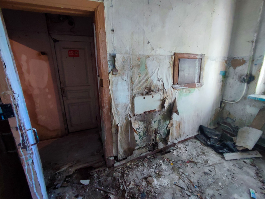 Обшарпанная комната с дверным проёмом, обрывками обоев и мусором на полу