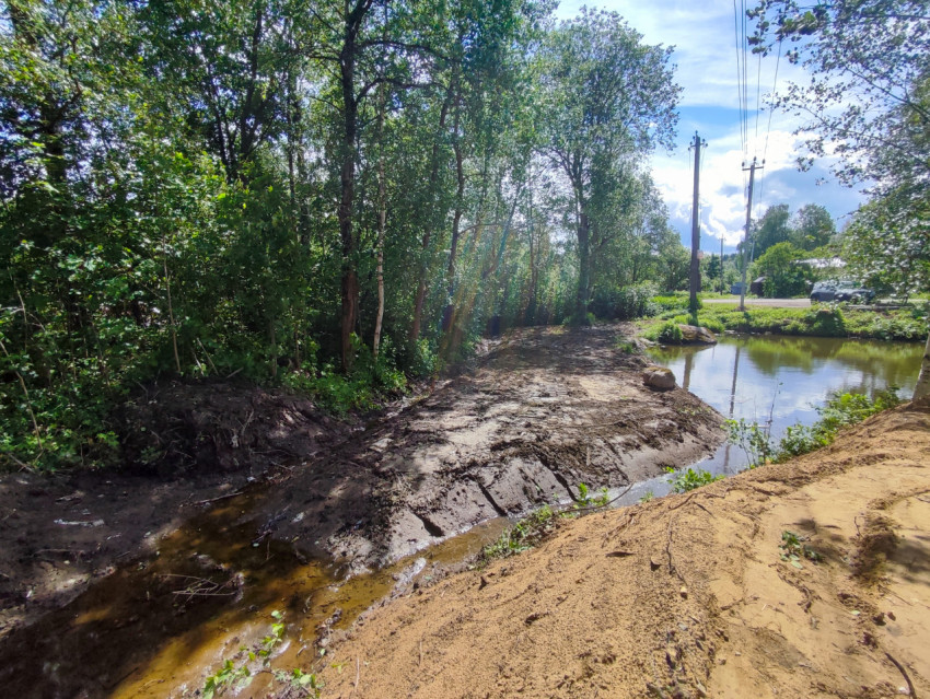 Разрытый берег пруда с протокой и насыпью песка после земляных работ