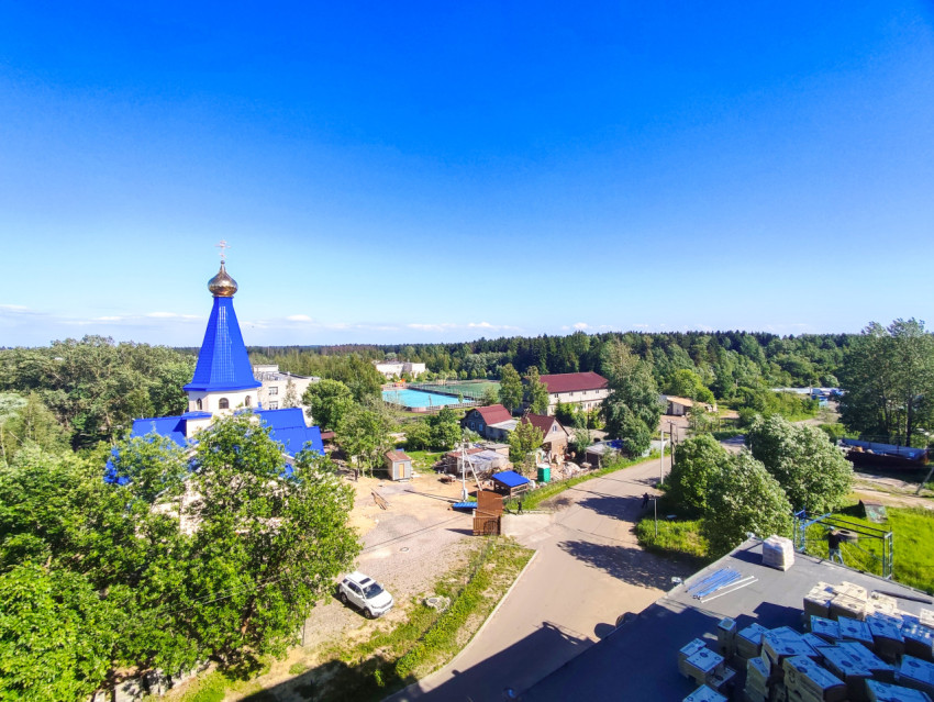 Панорама посёлка с православным храмом и стройматериалами на крыше на переднем плане