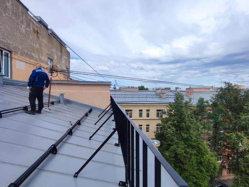 Фальцевая металлическая кровля с ограждением и проводами на фоне соседних домов