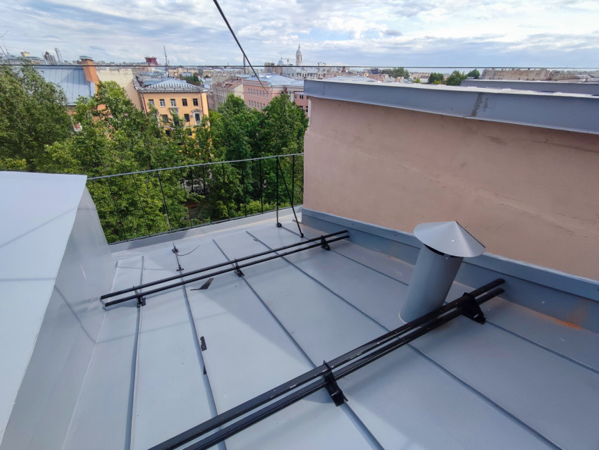 Участок металлической крыши с ограждением и снегозадержателями на фоне городской панорамы