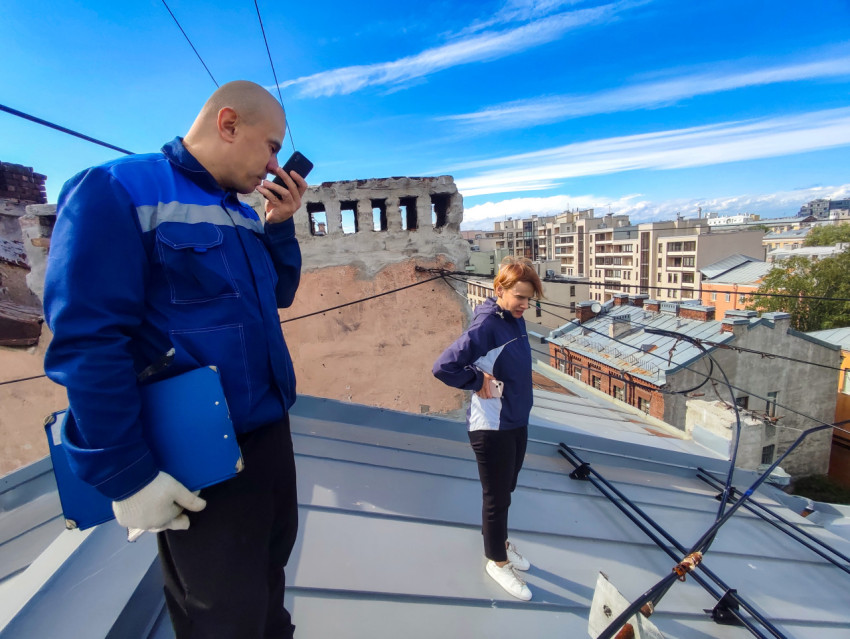 Двое сотрудников на крыше проводят осмотр кровли и коммуникаций на фоне городской застройки