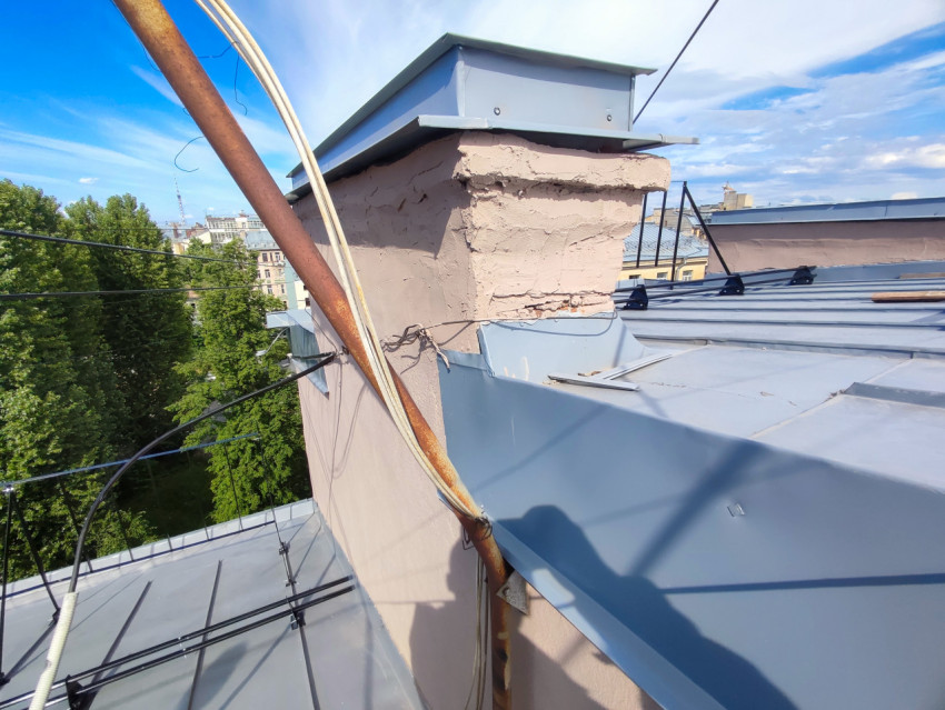 Вентиляционная шахта с металлическим колпаком и кабелями на фальцевой крыше