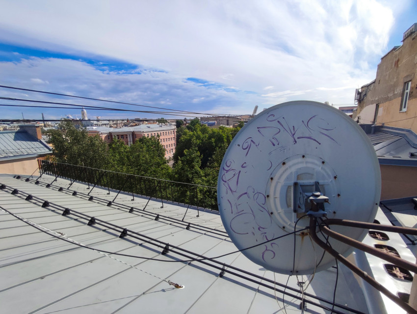 Спутниковая антенна на крыше и городской горизонт под облачным небом