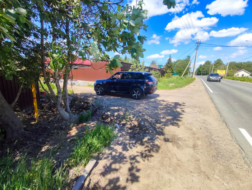 Тёмный внедорожник на грунтовом съезде у шоссе рядом с деревьями и линиями электропередачи