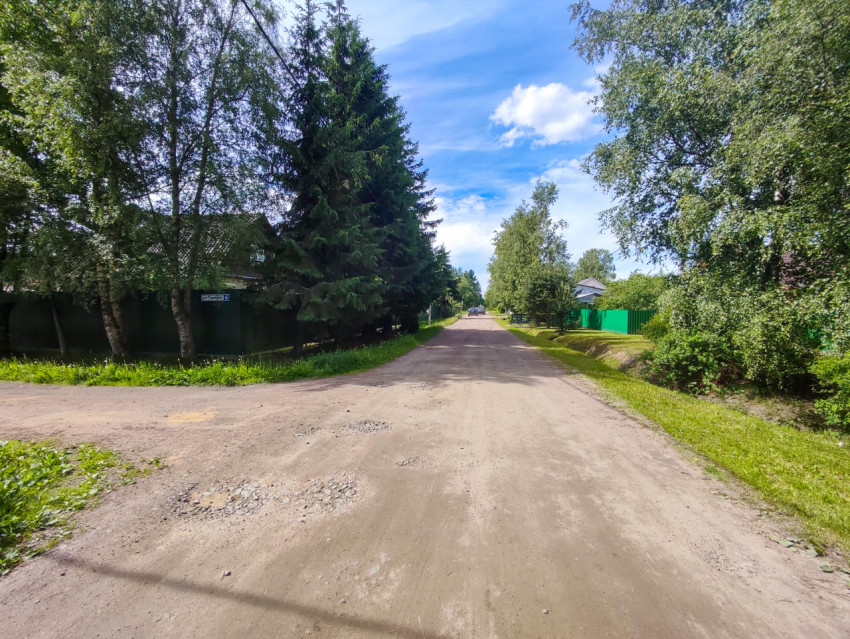 Перекресток грунтовых дорог с елью, зелёным забором и табличкой «ул. Полевая, 6»