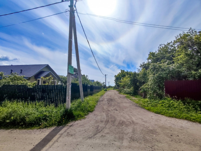Грунтовая дорога в поселке с опорой ЛЭП, проводами и ярким солнцем в небе