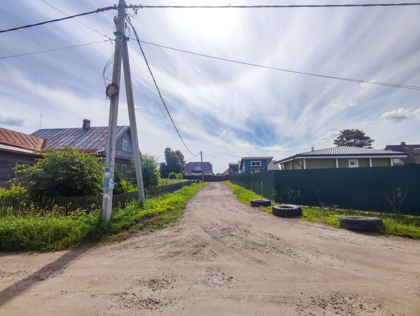 Грунтовая сельская улица с опорой ЛЭП, проводами и частными домами