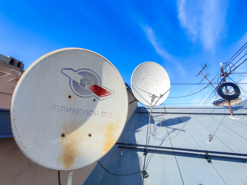 Две спутниковые тарелки и кабельные линии на крыше жилого дома