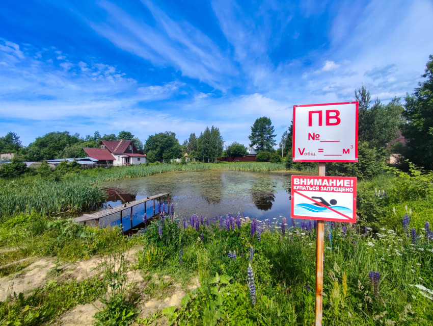 Широкий вид на сельский пруд с табличками пожарного водоёма и запретом купания