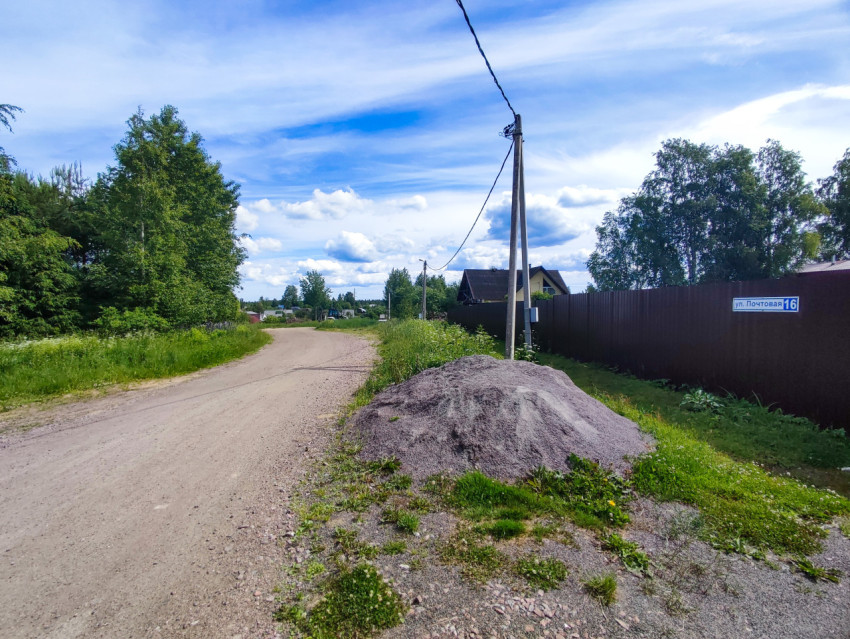 Просёлочная дорога с кучей гравия у забора и опорами электросети