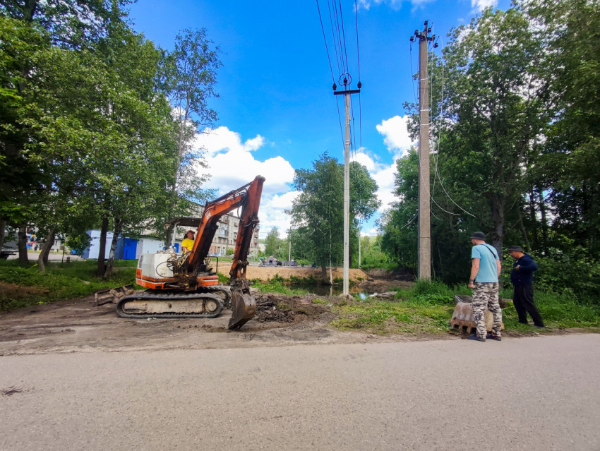Мини-экскаватор на гусеницах и рабочие у траншеи рядом с опорами линии электропередачи