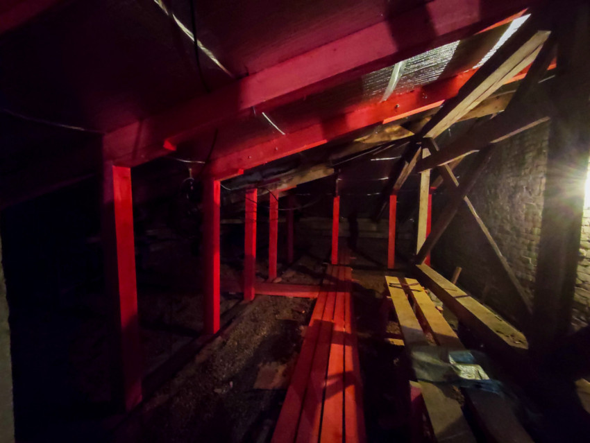 Подкровельное пространство с красными деревянными подпорками, досками и кирпичной стеной во время ремонта