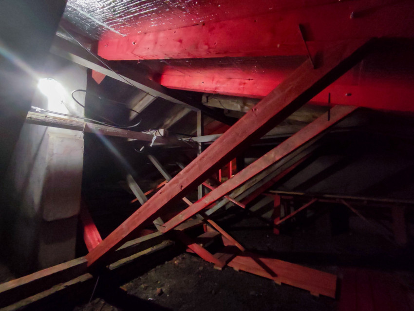 Чердачное помещение с красными балками, проводкой и обломками досок