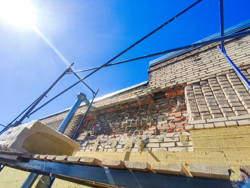 Участок кирпичной стены с повреждённой кладкой и утеплителем на строительных лесах