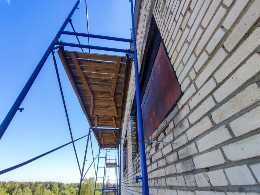 Строительные леса с деревянным настилом у кирпичной стены и металлическим щитом