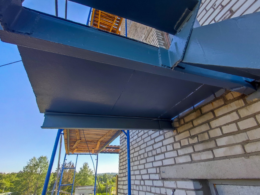 Нижняя сторона металлической площадки и балки каркаса у кирпичной стены рядом со строительными лесами