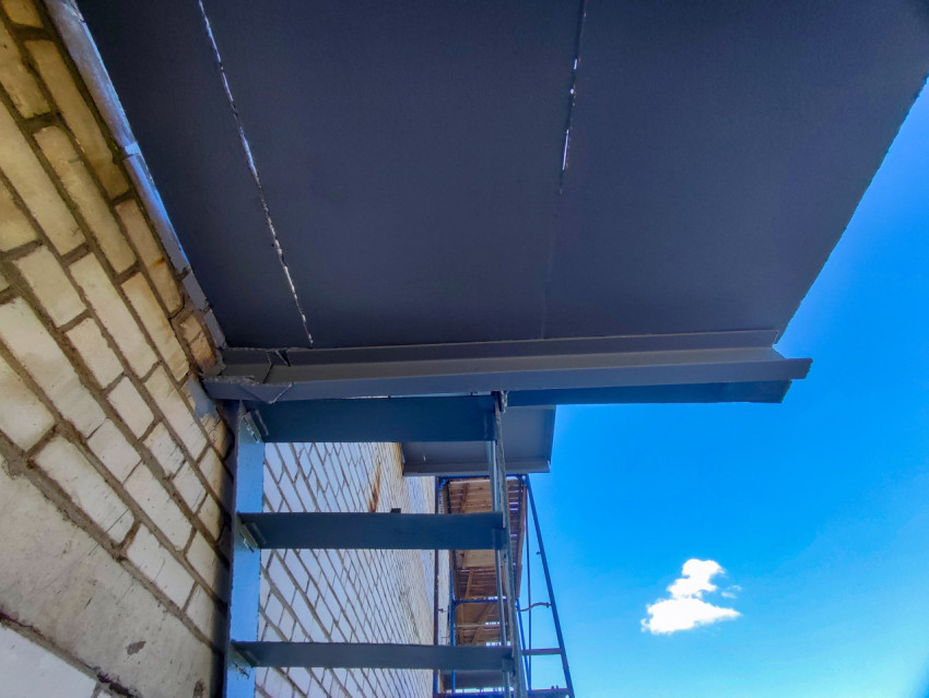 Консольные балки и нижняя плоскость металлического навеса у кирпичной стены на фоне синего неба