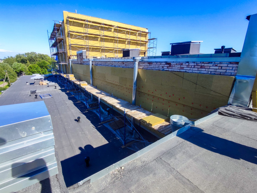 Строительные леса и утепление фасада вдоль плоской кровли с водостоками