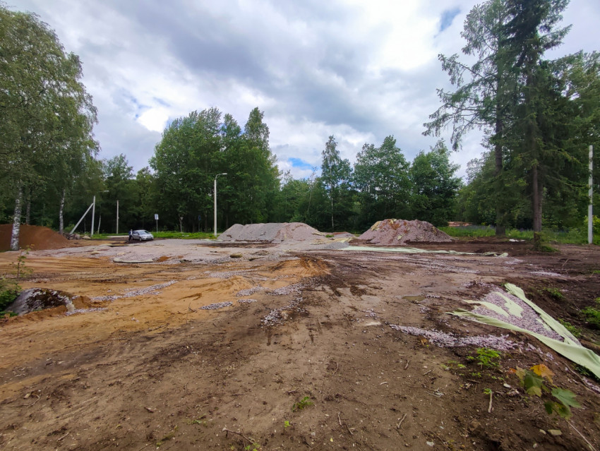 Площадка земляных работ с кучами щебня и песка у лесополосы
