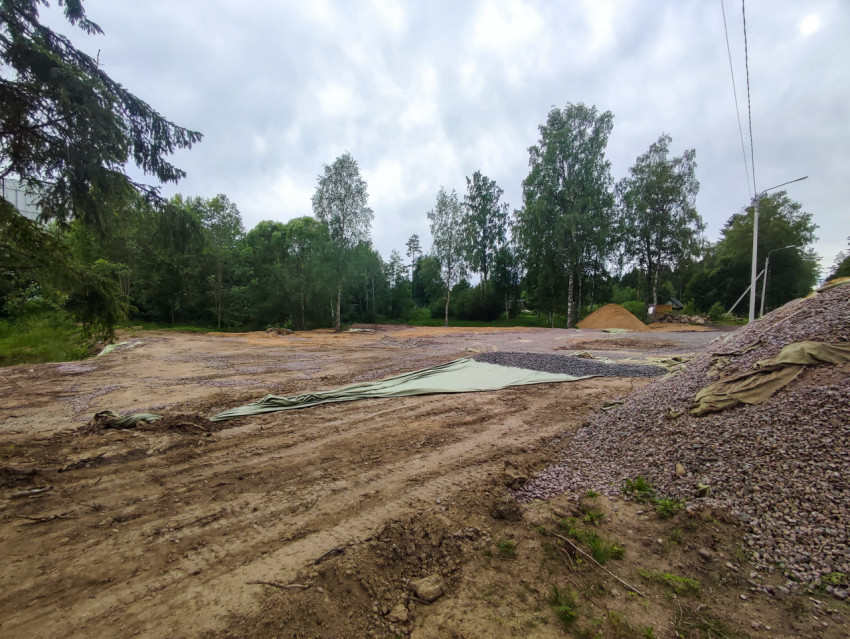 Строительная площадка с грунтовой планировкой и кучами щебня и песка у леса