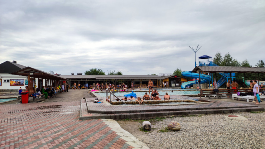 Открытый бассейн с водной горкой и отдыхающими на территории комплекса