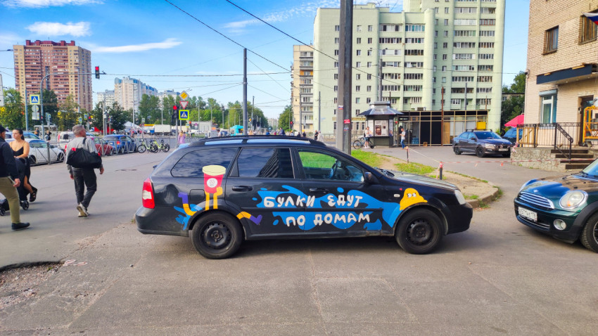 Легковой автомобиль с яркой рекламной надписью и рисунком стакана напитка на городской улице