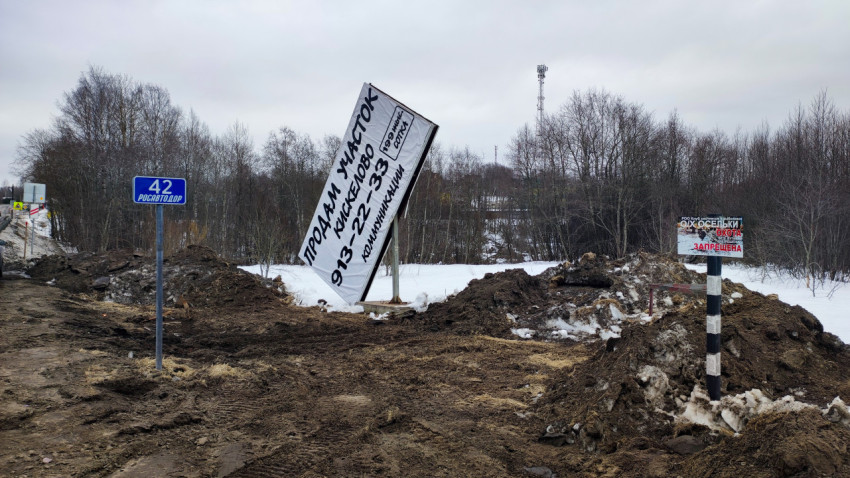 Повреждённый рекламный щит и знаки у обочины дороги зимой