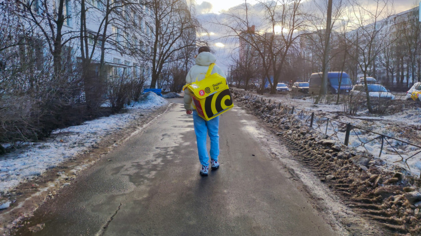 Курьер Яндекс Еда идет по зимней улице с заказом