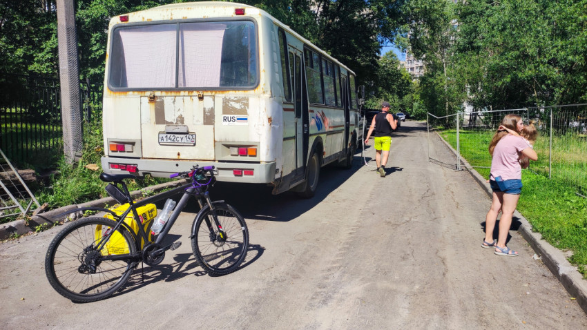Автобус с потёртым кузовом и велосипед с жёлтым багажом на асфальтовой дороге у ограждения