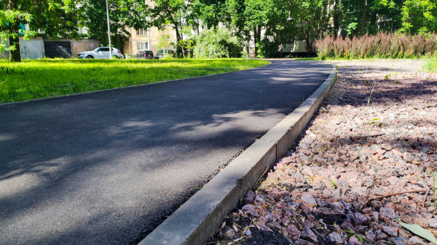 Изогнутая асфальтовая дорожка с высоким бордюром у зоны озеленения во дворе