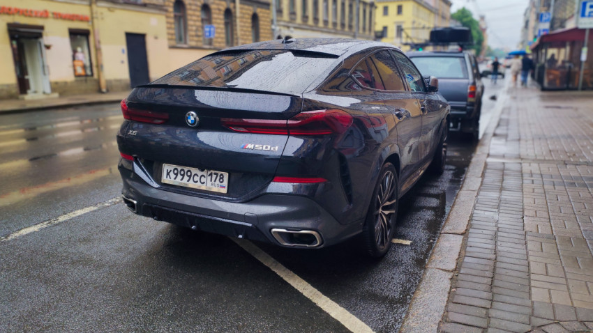 BMW X6 M50d на мокрой улице в городской застройке, вид сзади