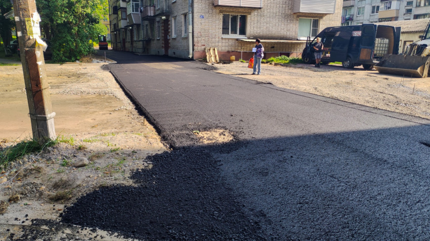 Свежий асфальт во дворе, жильцы у дома и строительная техника на участке ремонта