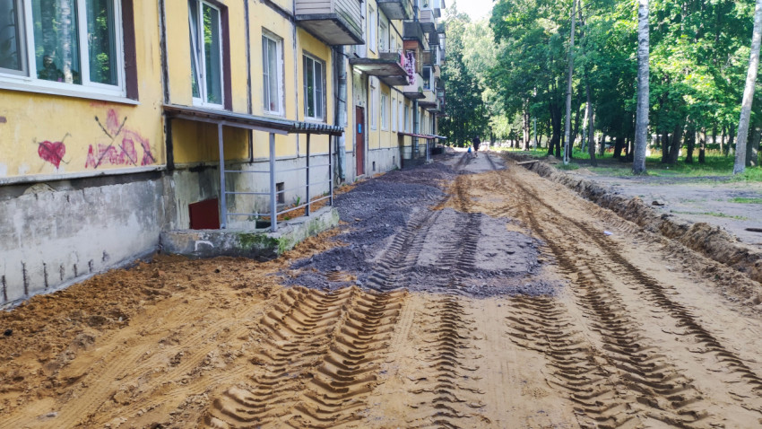 Временная грунтовая дорога вдоль дома с колеёй и траншеей на участке дворового ремонта